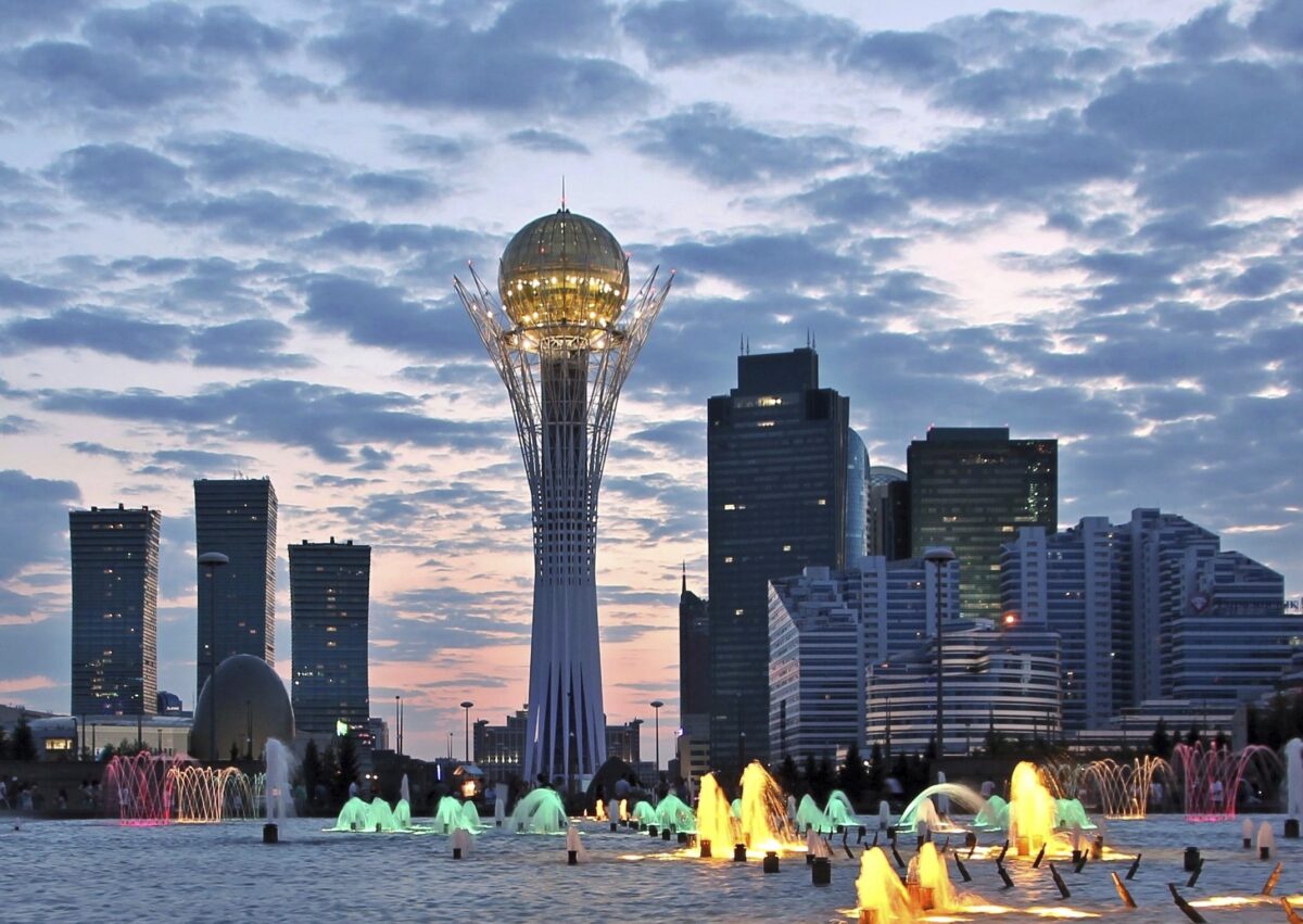 Bayterek Tower in Astana illuminated at dusk with city skyline and colorful fountains in the foreground